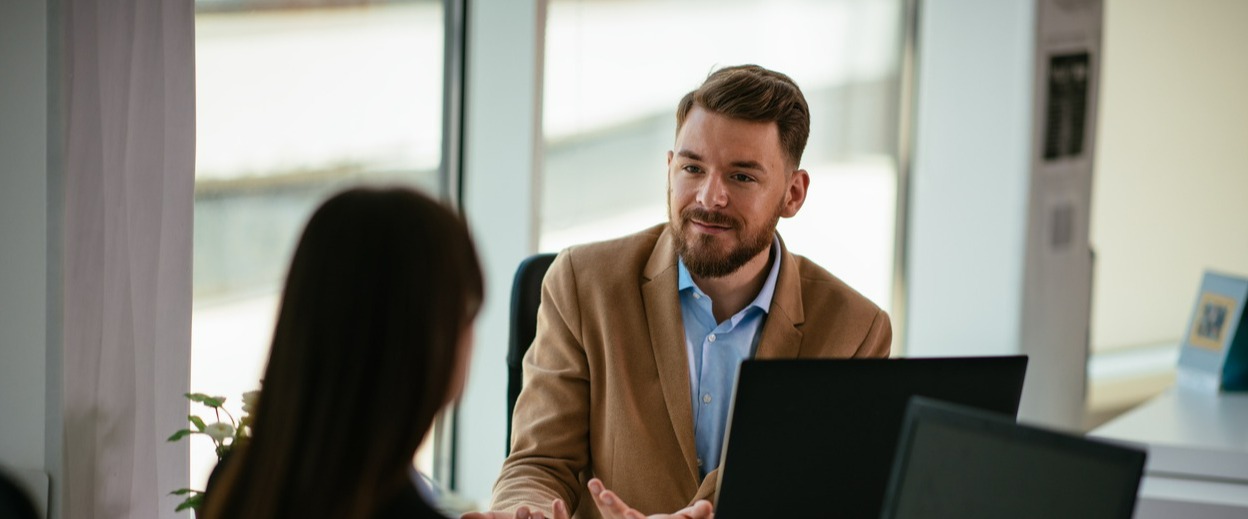 two adults seated at a desk smiling and talking 