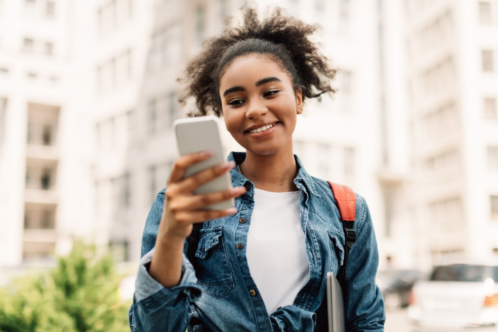 cheerful african american student girl on phone standing outside